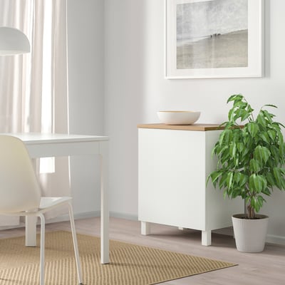 Moble d'emmagatzematge BESTÅ blanc amb prestatges regulables, al costat d'una planta verda, apte per a espais reduïts.