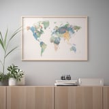 L'obra d'art emmarcada del mapa del món penja a la paret sobre la prestatgeria de fusta amb plantes i llibres.