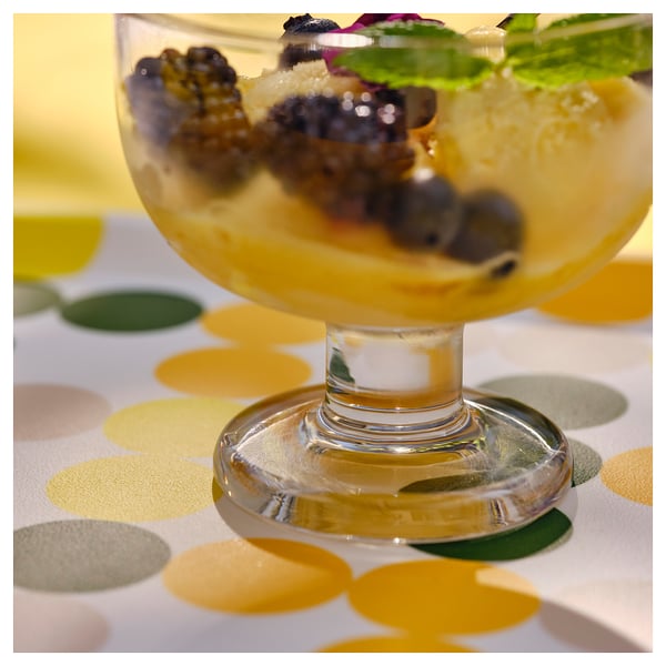 Bol de postres de vidre transparent amb fruita, menta i gelat. Base de tija elegant, fons d'estovalles de lunars.