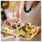 Una persona sosté una safata de lunars amb dos bols de postres de vidre farcits de gelats i baies, decorats amb flors comestibles.