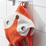 Una tovallola infantil amb caputxa de guineu penja d'un ganxo, mostrant el seu disseny càlid i absorbent.