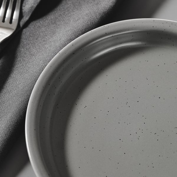 Primer pla en blanc i negre d'un plat de gres texturitzat i tacat sobre un drap gris, que mostra la seva qualitat rústica i artesanal.