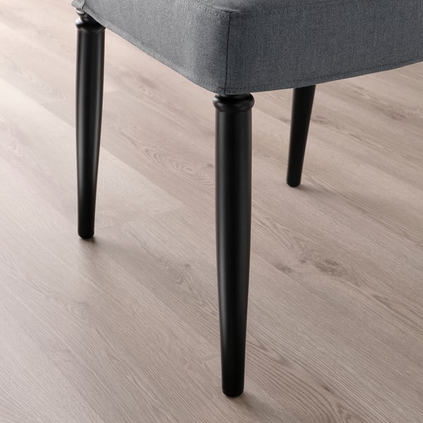 Cadira de menjador d'alta qualitat amb teixit gris fosc i potes resistents de metall negre. Es mostra sobre terra de fusta clara.