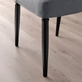 Cadira de menjador d'alta qualitat amb teixit gris fosc i potes resistents de metall negre. Es mostra sobre terra de fusta clara.