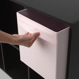 Obre a mà una caixa d'emmagatzematge de color rosa clar des d'un prestatge fosc, ideal per a l'emmagatzematge organitzat.