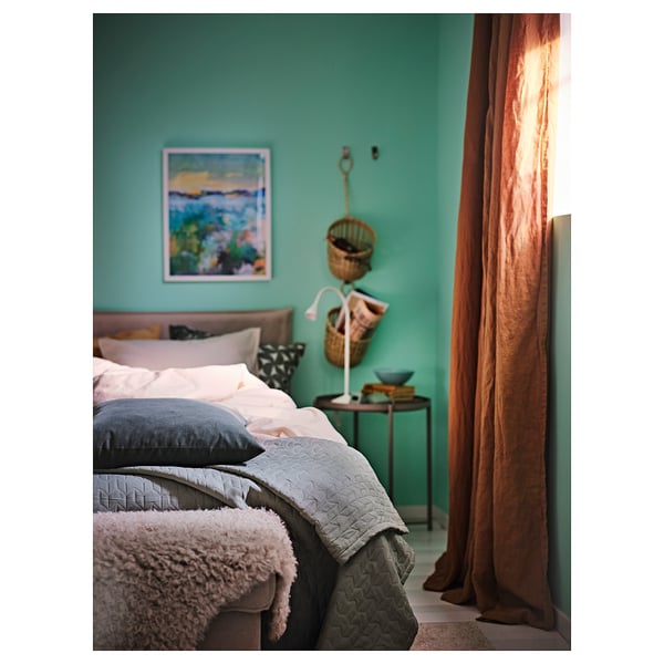 Dormitori acollidor amb parets verda verda, llit gris, art, cistelles, taula de fusta i cortines taronja.
