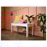 Banc blanc EKEDALEN contra paret rosa amb coixins grocs, rosa, planta i llibres.