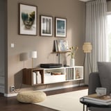 Sala d'estar moderna amb prestatge EKET, tocadiscs, llibres, llum i art. Sofà gris, llum de peu i persianes al costat de la finestra.