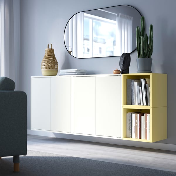 Sala d'estar moderna amb emmagatzematge EKET blanc i groc clar contra la paret, mirall a sobre, objectes decoratius i cadira grisa.