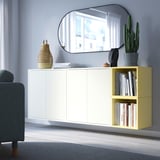 Sala d'estar moderna amb emmagatzematge EKET blanc i groc clar contra la paret, mirall a sobre, objectes decoratius i cadira grisa.