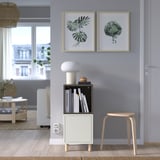 Sala d'estar moderna amb prestatges EKET grisos, llibres, llum, estampats i taula de centre de vímet, llum natural.