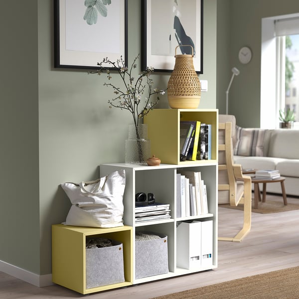 Habitació moderna amb paret verda, emmagatzematge groc EKET, llibres i gerros, decoració acollidora.