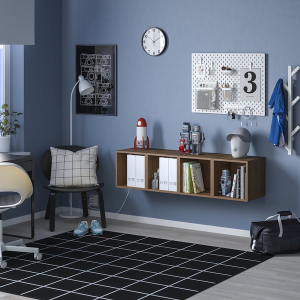 Habitació blava minimalista amb prestatgeria EKET marró, llibres, joguines, rellotge, cartell, penjador, taula, cadira i catifa en blanc i negre.