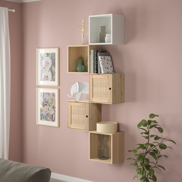 Prestatges EKET de fusta amb armaris oberts i tancats. Varia de mida, amb llibres, gerros i decoració. El fons de paret de color rosa clar crea una pantalla acollidora.