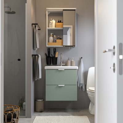 Bany modern amb armari ENHET. Mirall corredís, accessoris negres, tovalloles grises. Lavabo blanc, dutxa.