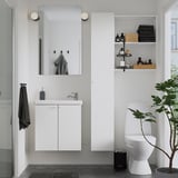 Bany modern i minimalista amb tocador blanc, mirall i detalls negres. La planta en test afegeix vegetació.