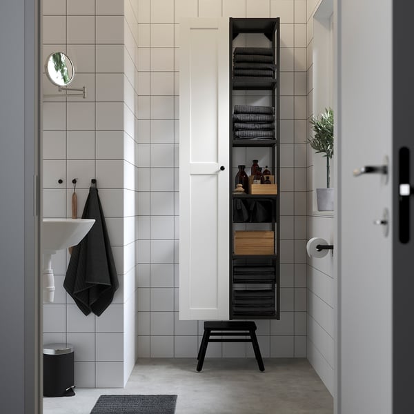 Bany modern amb armari alt blanc i prestatgeria oberta. Compacte però espaiós, conté tovalloles, ampolles i decoració. Accents negres.