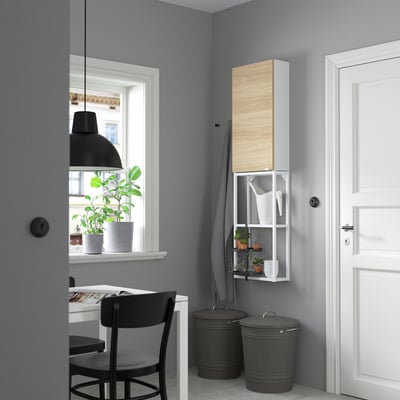 Oficina minimalista a casa amb armari blanc, escriptori i cadira negra. Estètica moderna amb planta en test i vista a la finestra.