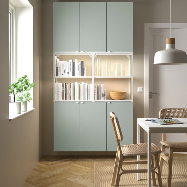 Sala d'estar moderna amb unitat d'emmagatzematge ENHET de color verd clar, amb llibres i decoració; Petita taula de menjador de fusta amb cadires.