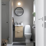 Bany modern amb tocador de roure ENHET, 2 calaixos, lavabo blanc, mirall rodó, vàter de paret, parets grises.