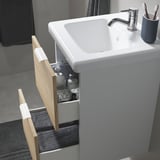 Armari de bany modern amb calaix obert amb articles de tocador i lavabo amb aixeta.