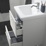Armari de lavabo de bany modern amb calaixos, articles de tocador i una catifa grisa a sota.