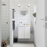 Bany blanc modern: tocador elegant amb mirall, rajoles grises, dutxa de vidre, planta i tovalloles.