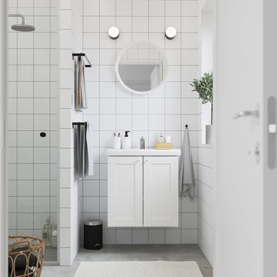 Bany blanc modern: tocador elegant amb mirall, rajoles grises, dutxa de vidre, planta i tovalloles.