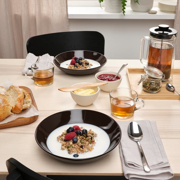 Taula amb dos bols de granola, baies, tasses de te, pa i una tetera. Els plats profunds contenen l'esmorzar.