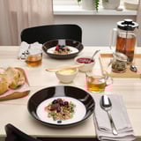 Taula amb dos bols de granola, baies, tasses de te, pa i una tetera. Els plats profunds contenen l'esmorzar.