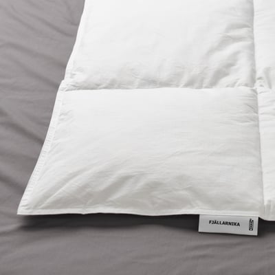 Un primer pla d'un nòrdic fjällräven blanc sobre roba de llit grisa, que mostra el seu teixit suau i nítid i el seu disseny cosit.