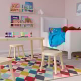 Habitació infantil amb taula i tamborets FLISAT. Fusta de fusta clara, de mida petita, de colors. Llibres i joguines a prop.