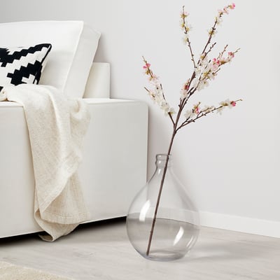 Gerro de vidre transparent que sosté una branca de flors al costat del sofà blanc.
