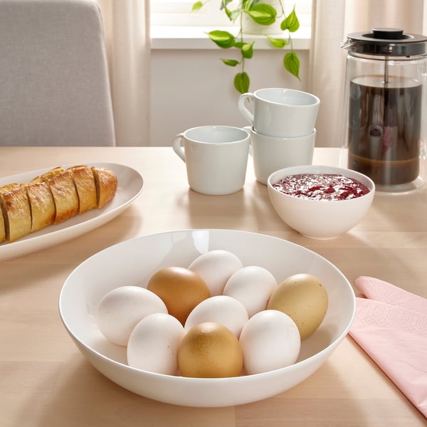 Un bol d'ous de colors barrejats es troba a la taula del menjador envoltat de pa, tasses de cafè i fruita, que suggereix l'esmorzar.
