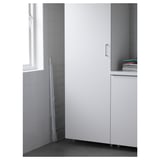 L'estenedor metàl·lic es recolza contra la paret, al costat d'un gran armari blanc. Perfecte per assecar la roba a l'interior o a l'exterior.