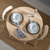 Petita taula de menjador rodona amb dues cadires de fusta clara, plats blancs, tovallons grisos i tovallons estampats.