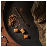 Un plat negre amb caramels de caramel, molles i una beina de vainilla. Fons de paper marró.