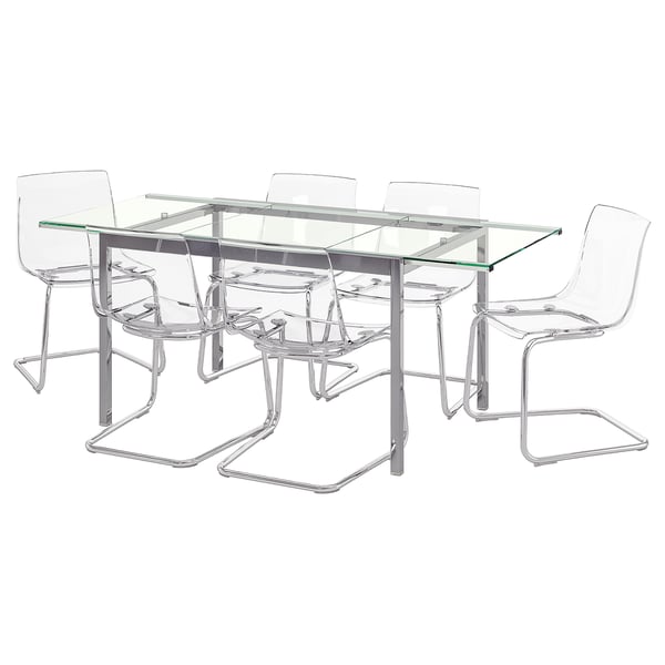 Taula de menjador moderna amb tapa de vidre amb quatre cadires de plàstic transparent, potes cromades, disseny elegant i minimalista.