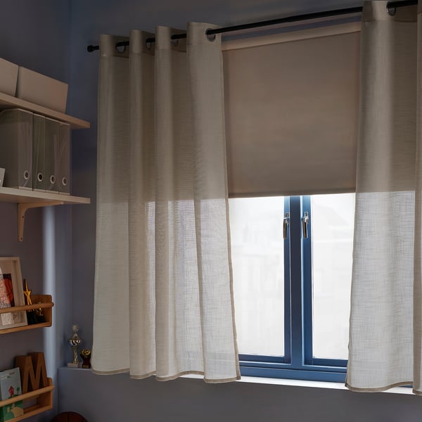 Cortines beix transparents pengen al costat de la finestra, fetes de polièster reciclat.
