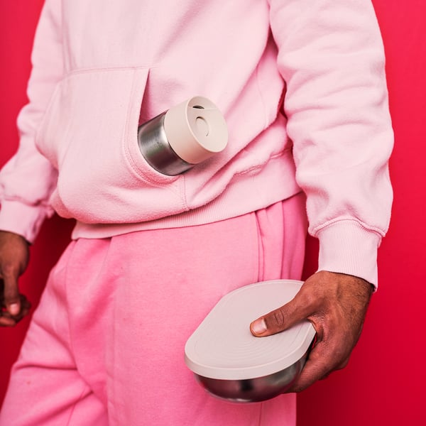 Persona amb vestit rosa sostenint envasos d'aliments blancs HALVVARM. Un és cilíndric, l'altre rodó amb tapa.