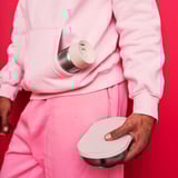 Persona amb vestit rosa sostenint envasos d'aliments blancs HALVVARM. Un és cilíndric, l'altre rodó amb tapa.