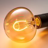 Primer pla d'una bombeta led càlida i brillant amb filament complex en una carcassa de vidre marró arrodonida, part d'un llum de peu elegant.