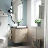 Tocador beix, lavabo semi-encastat, mirall rodó, disseny compacte.
