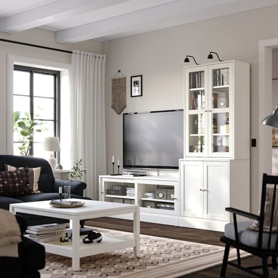 Sala d'estar moderna amb mobles HAVSTA, banc de TV de vidre, cortina negra, sofà fosc, catifa estampada, terra de fusta.