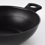 Wok negre amb recobriment antiadherent i nanses resistents sobre superfície blanca.