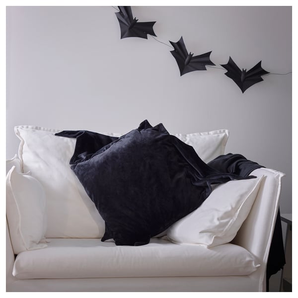 Sofà blanc amb coixins negres en forma de ratpenat, un amb cremallera, per a la decoració de Halloween.