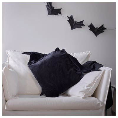 Sofà blanc amb coixins negres en forma de ratpenat, un amb cremallera, per a la decoració de Halloween.
