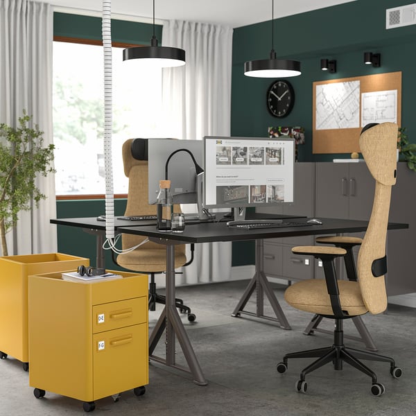 Oficina moderna amb escriptoris IDÅSEN, armaris grocs, cadires ergonòmiques, monitors i llums penjants.