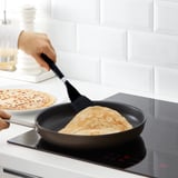La persona utilitza l'espàtula d'Ikea per donar la volta a les creps a la paella a la cuina d'inducció. Fons de cuina blanc.