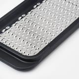 Primer pla del ratllador d'acer inoxidable en marc de plàstic negre, que mostra forats afilats i uniformement espaiats i un disseny durador.